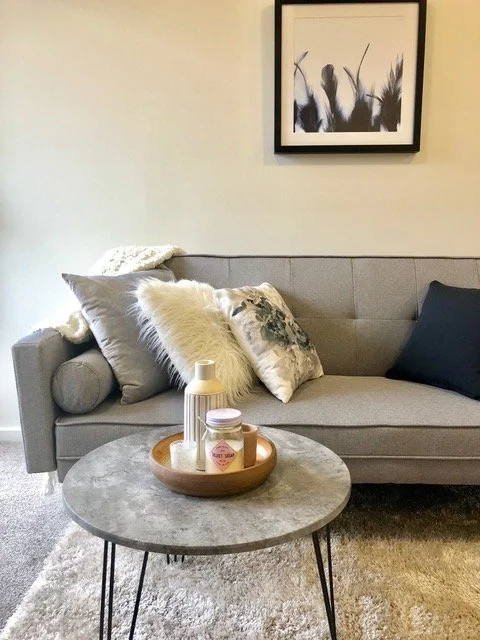 Living room with gray sofa, decorative pillows, a round coffee table with candles and a tray, framed modern artwork on the wall.