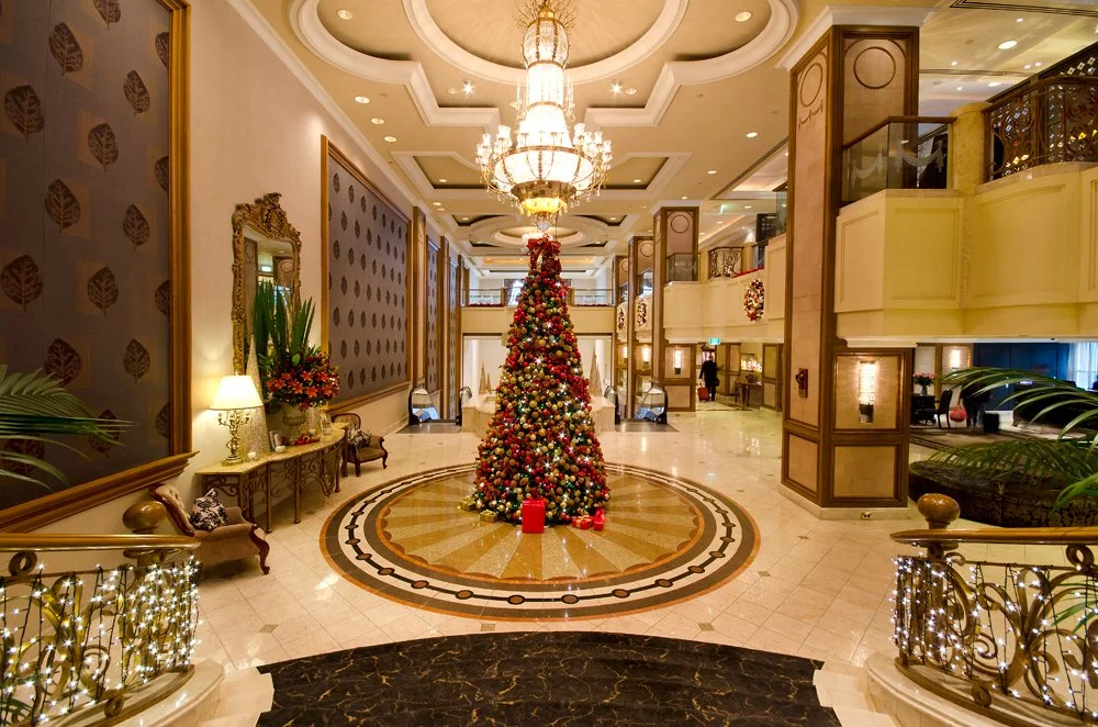Grand hotel lobby  at the Langham Hotel, decorated for Christmas with a central decorated tree, chandeliers, and holiday wreaths.
