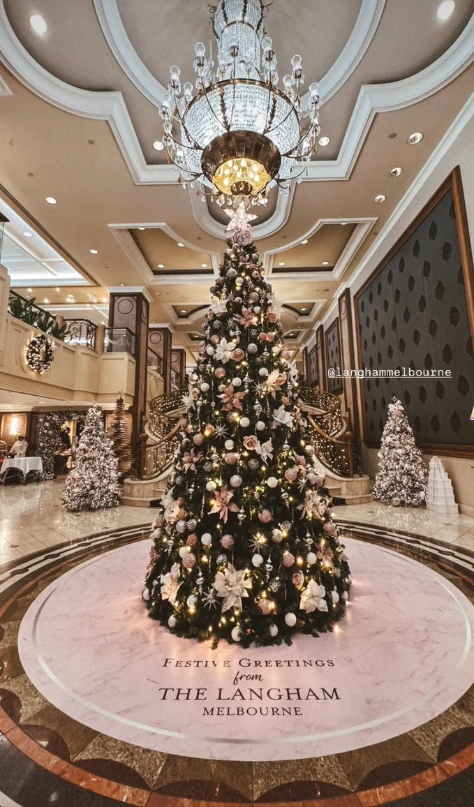 A decorated Christmas tree with a pink vinyl floor decal underneath reading Festive greetings From the Langham Hotel