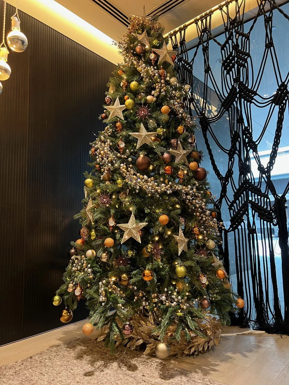Decorated Christmas tree with gold, bronze, and silver ornaments and star toppers in a modern interior.