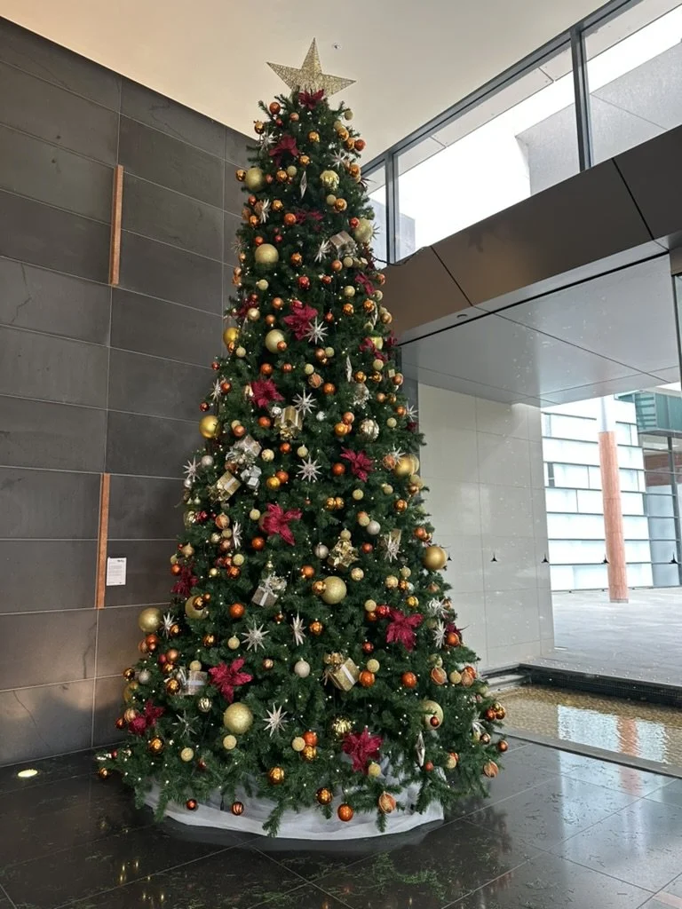 Decorated Christmas tree with gold, red, and white ornaments in a modern indoor space.