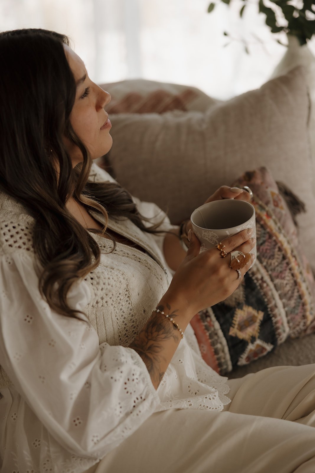 Woman sitting comfortably with a warm mug, reflecting in a peaceful home setting, representing the investment in therapy, emotional healing, and personal growth.