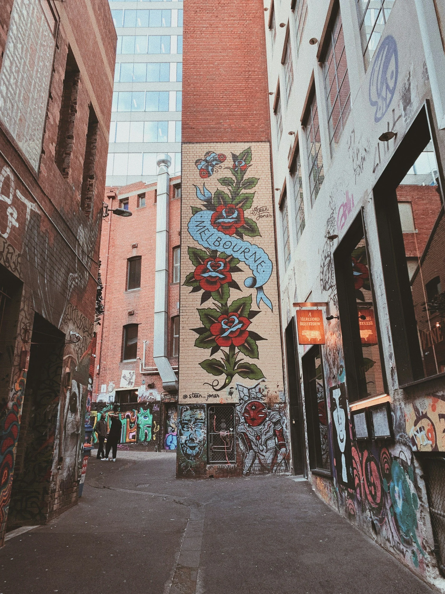 A narrow urban alleyway surrounded by graffiti-covered brick and concrete buildings, with people walking.