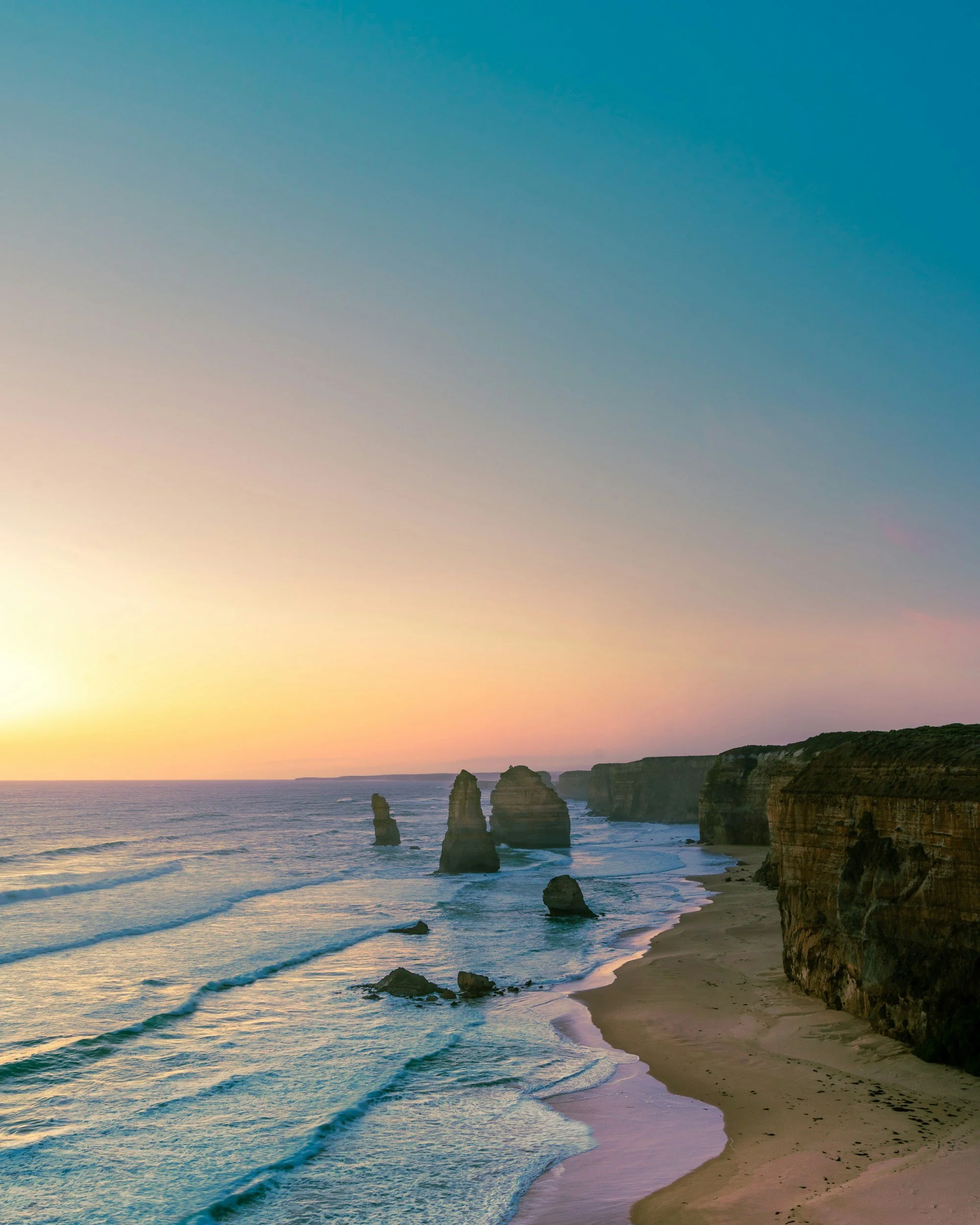 A sunset over Australia’s Twelve Apostles limestone stacks along the Great Ocean Road, with cliffs on the right and the ocean on the left.
