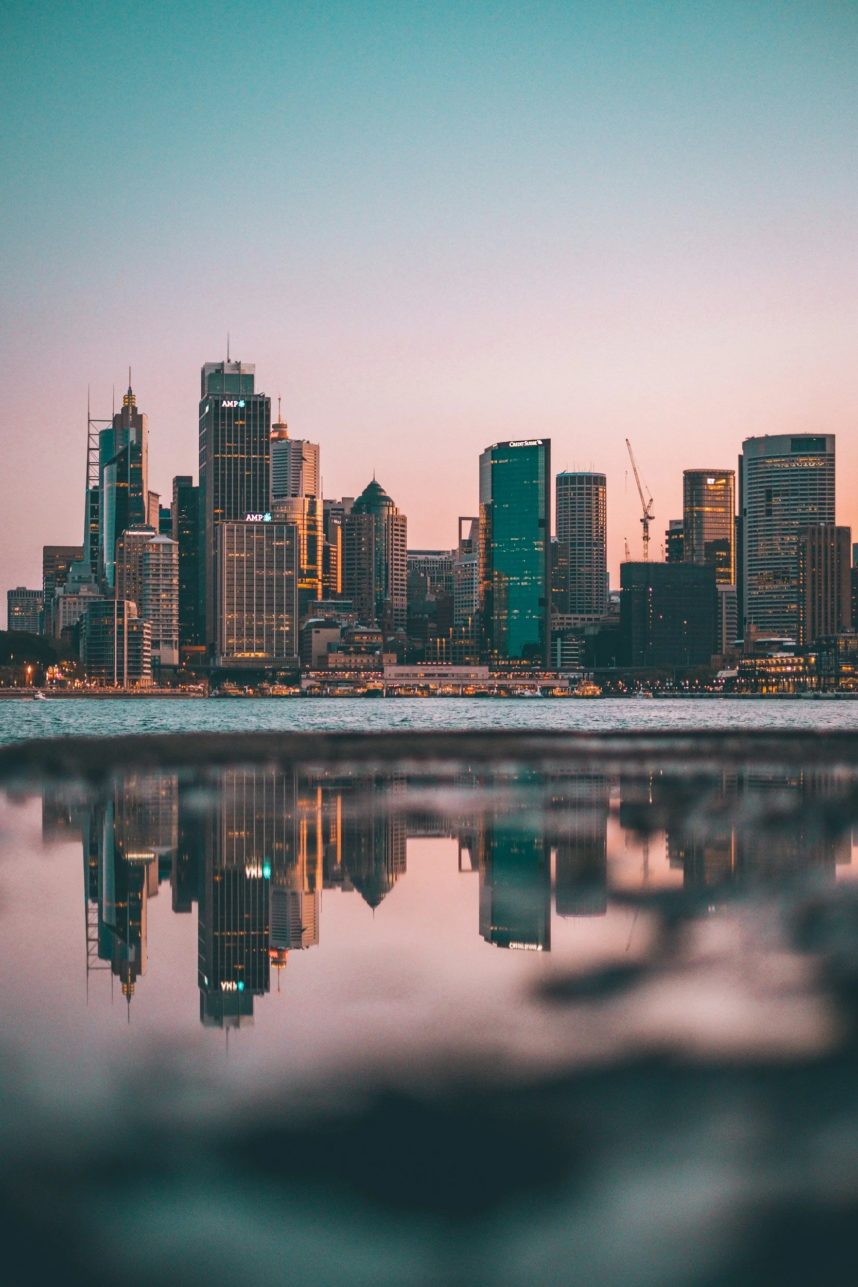 City skyline at sunset with skyscrapers reflected in the water.