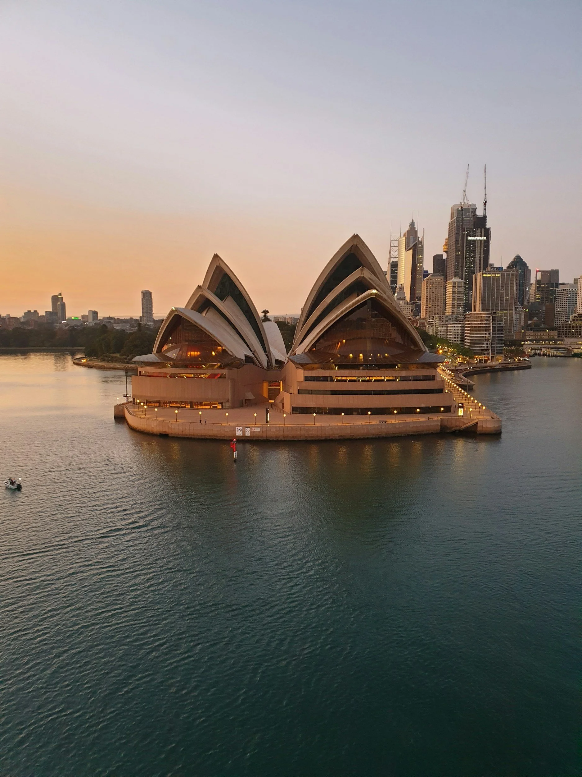 Sydney Opera House with city skyline and water at sunset.
