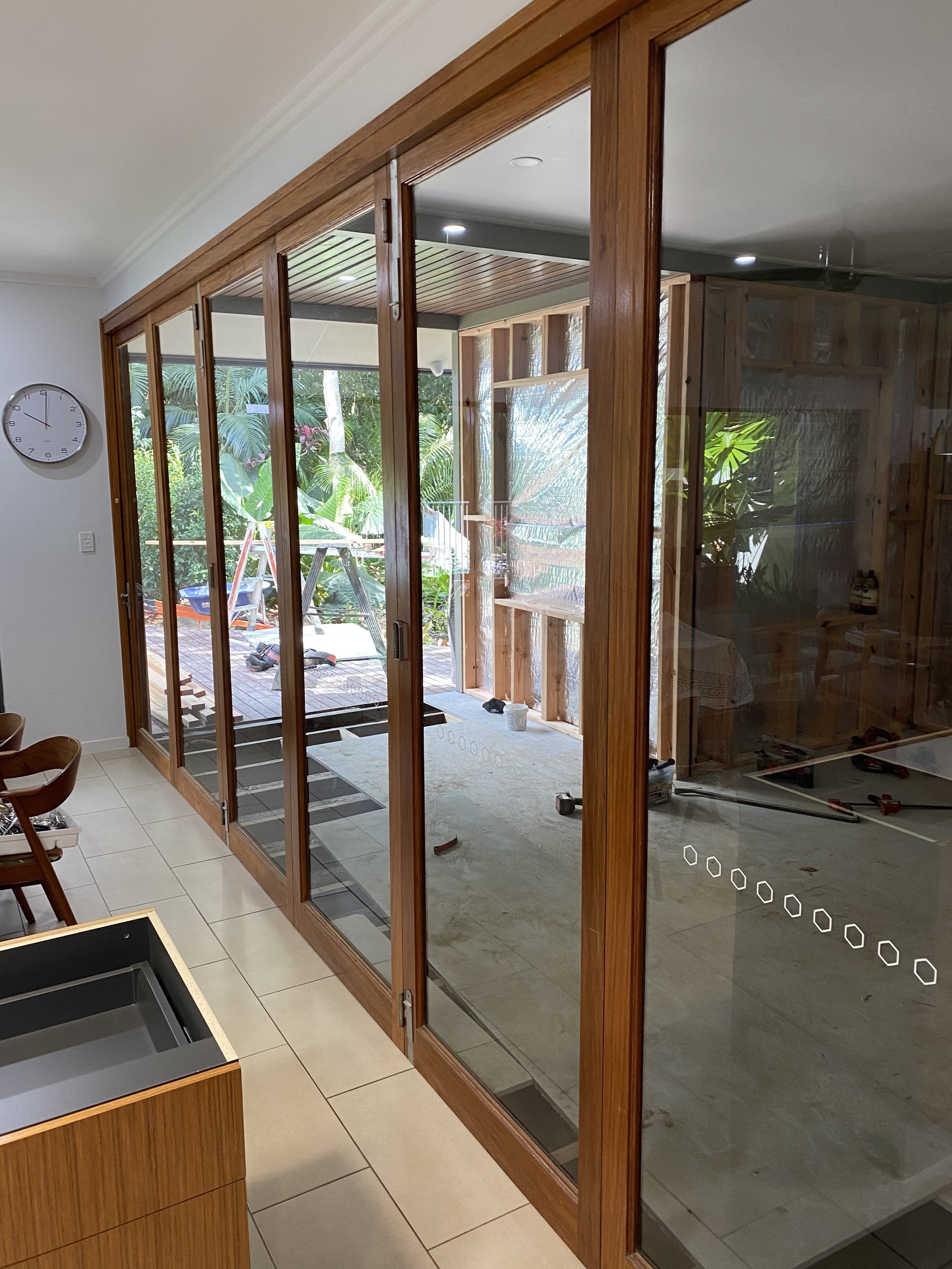 Room with a glass enclosure under construction, showing wooden frames, construction tools, and greenery outside.