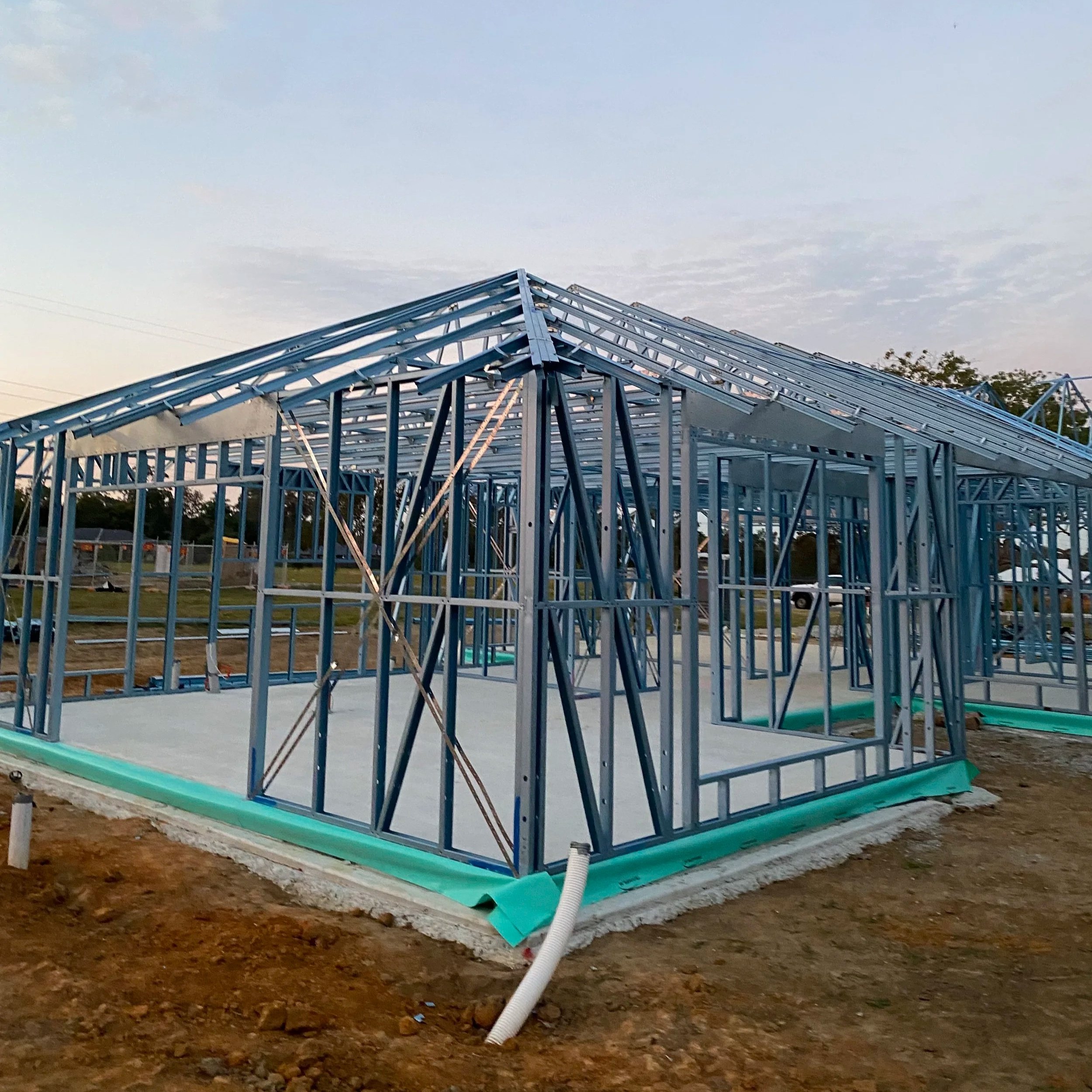 Steel framing structure for a building under construction at dusk, with the sky visible in the background.
