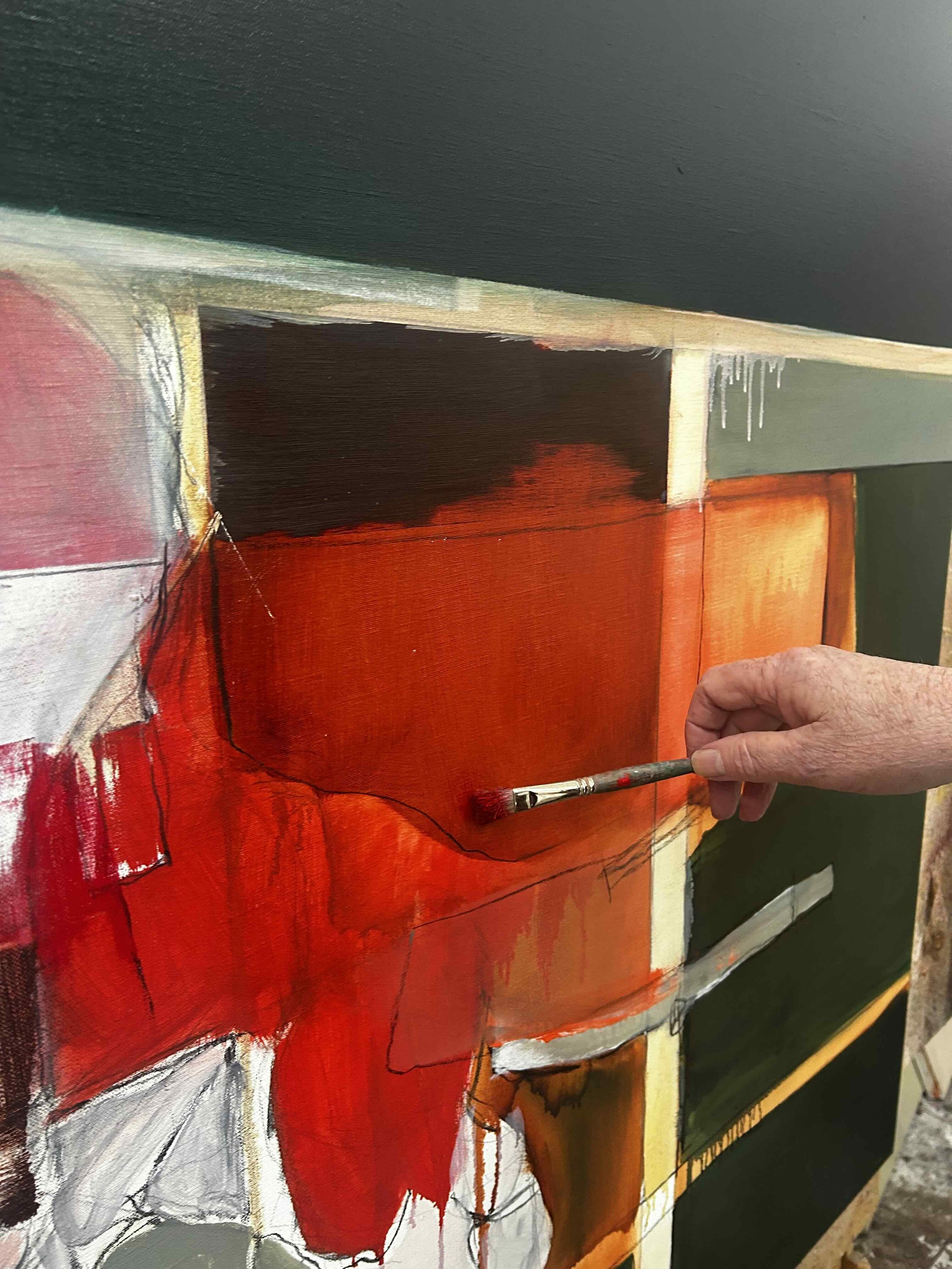 Close-up of an artist painting a colorful abstract canvas with red, black, yellow, and white hues, using a paintbrush.