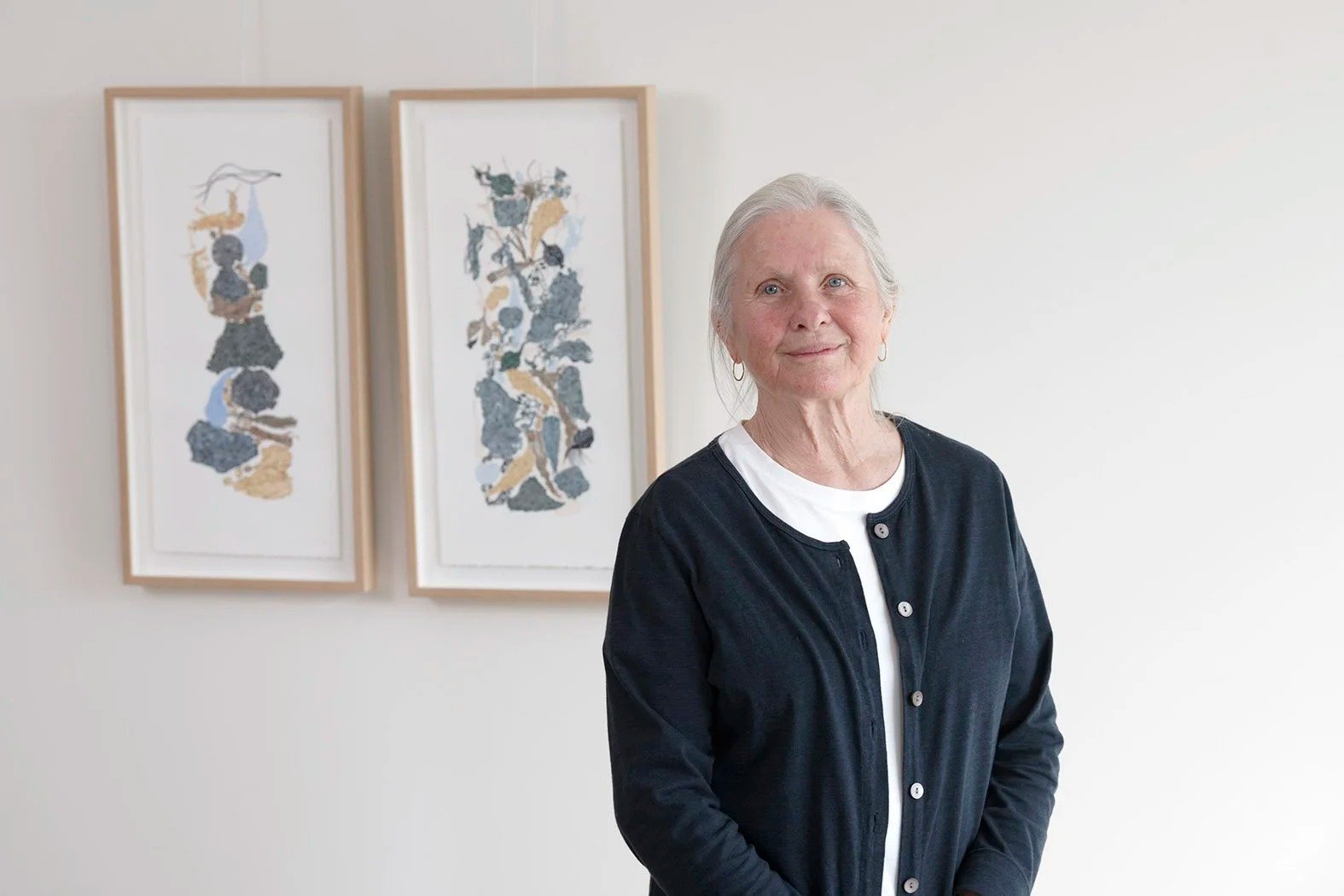 Artist Clare Bell standing in front of two of her framed works