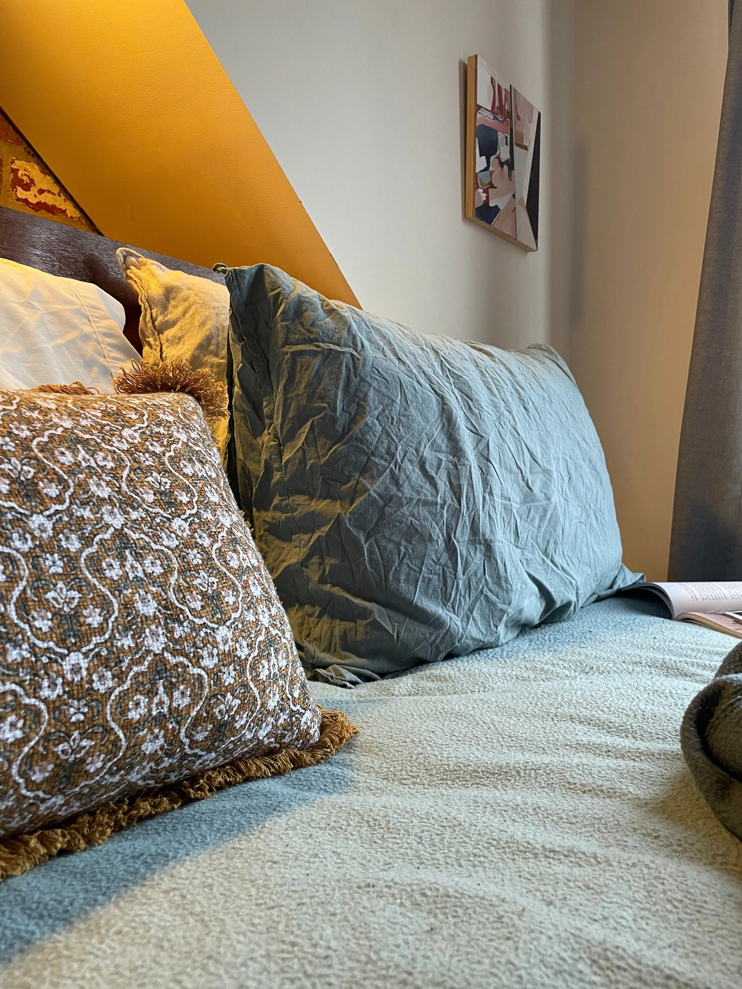 Close-up of a cozy bed with a beige carpet and decorative pillows, set against a colorful wall with artwork.