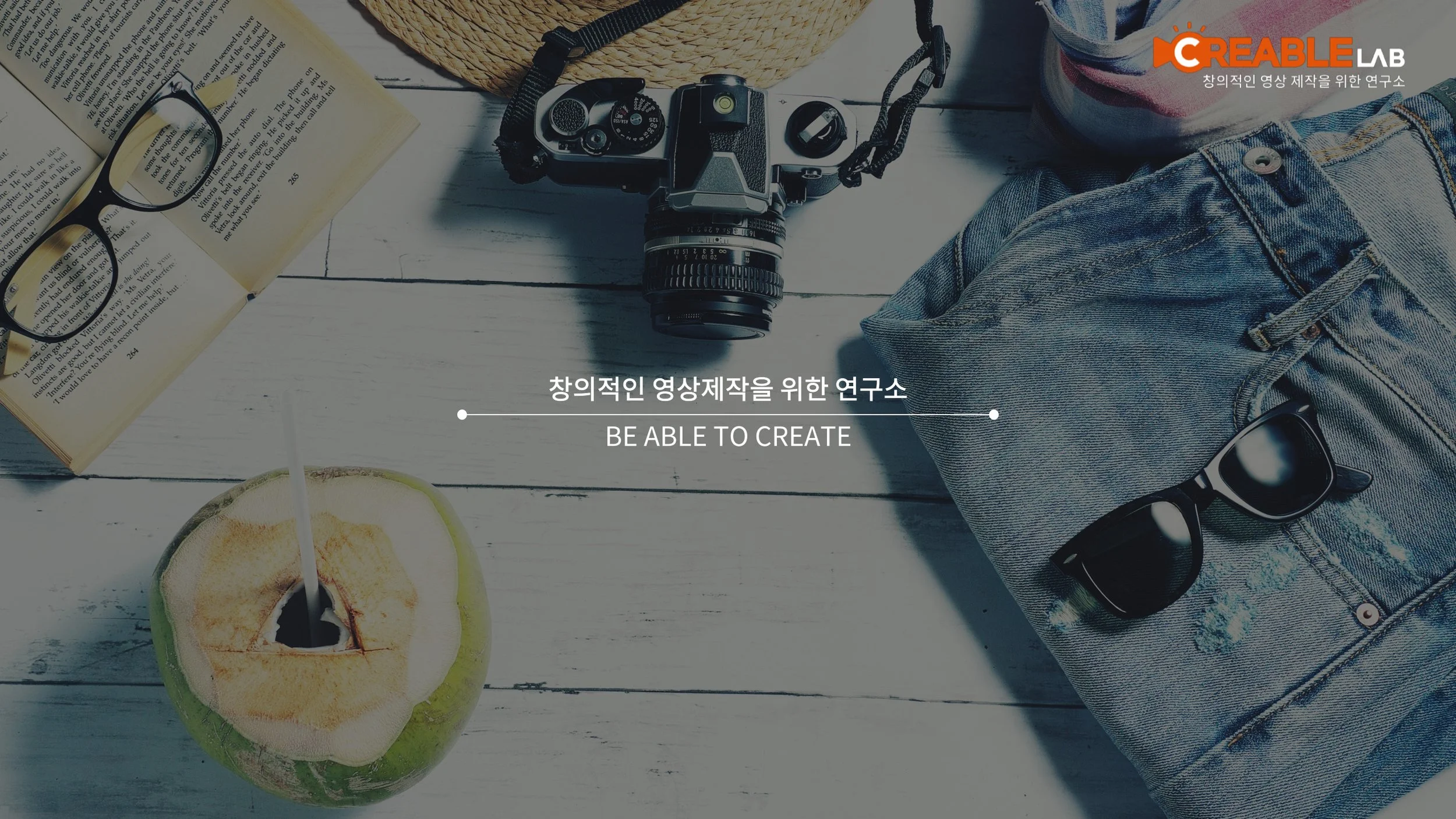 여행 용품과 책, 안경, 카메라, 선글라스, 코코넛 과일과 파인애플이 휴양지의 테이블 위에 놓여 있는 모습.