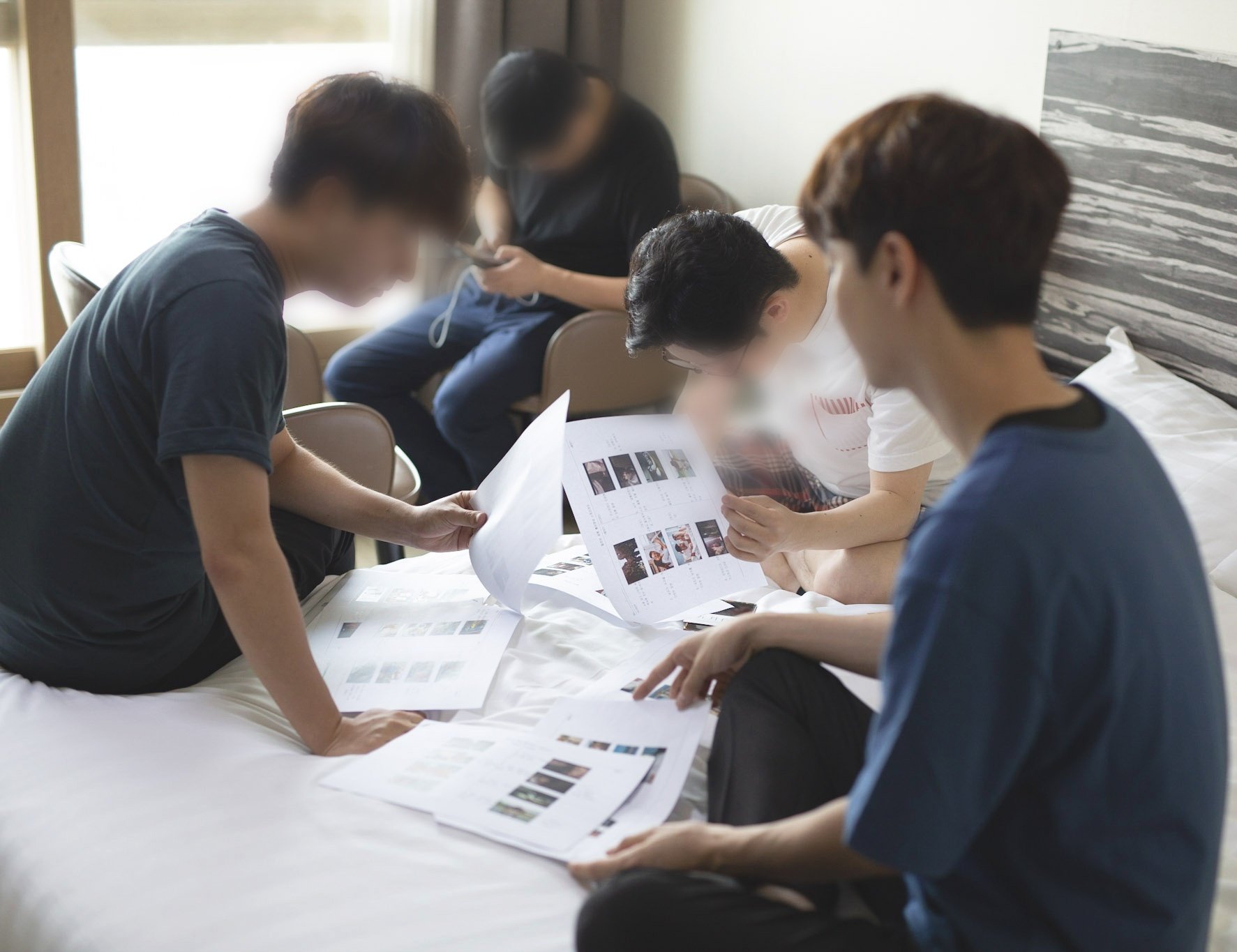Group of people reviewing printed documents and photos together on a bed
