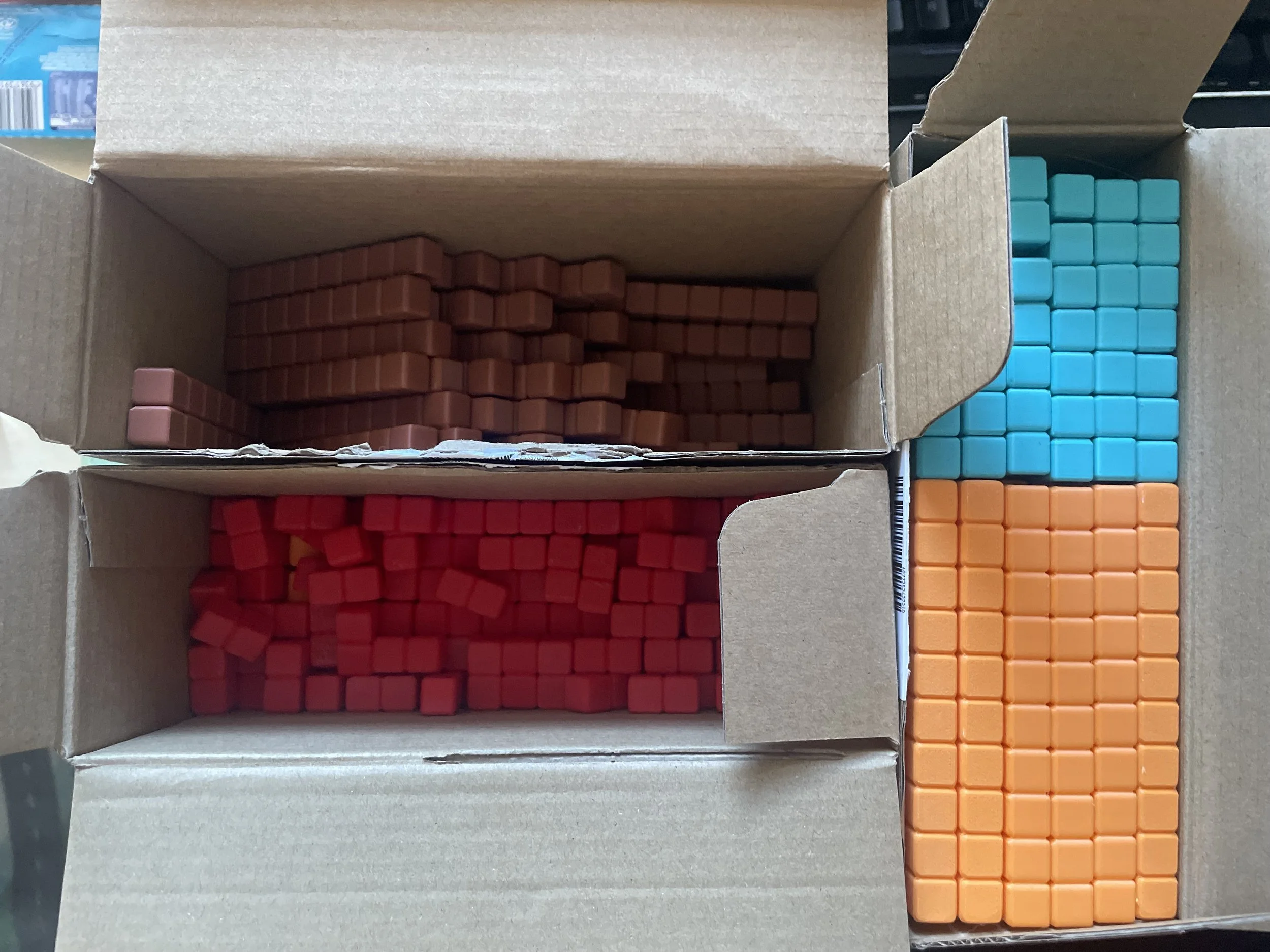 Stacked boxes containing packs of colorful Rubik's cubes in orange, red, blue, and brown colors.