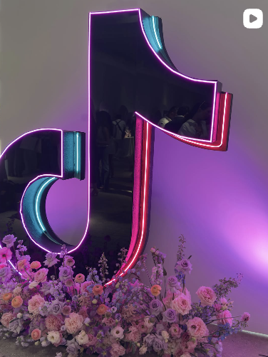 Neon pink, purple, and blue letter J illuminated with flowers at the base.