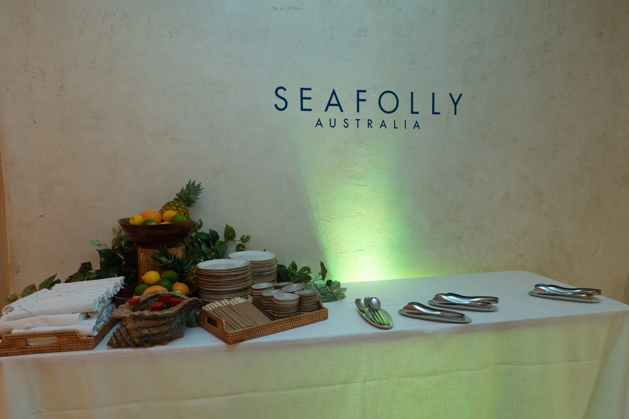Buffet table with fruit, plates, and utensils at a restaurant in Australia, with a sign reading 'Seafoily Australia' on the wall.