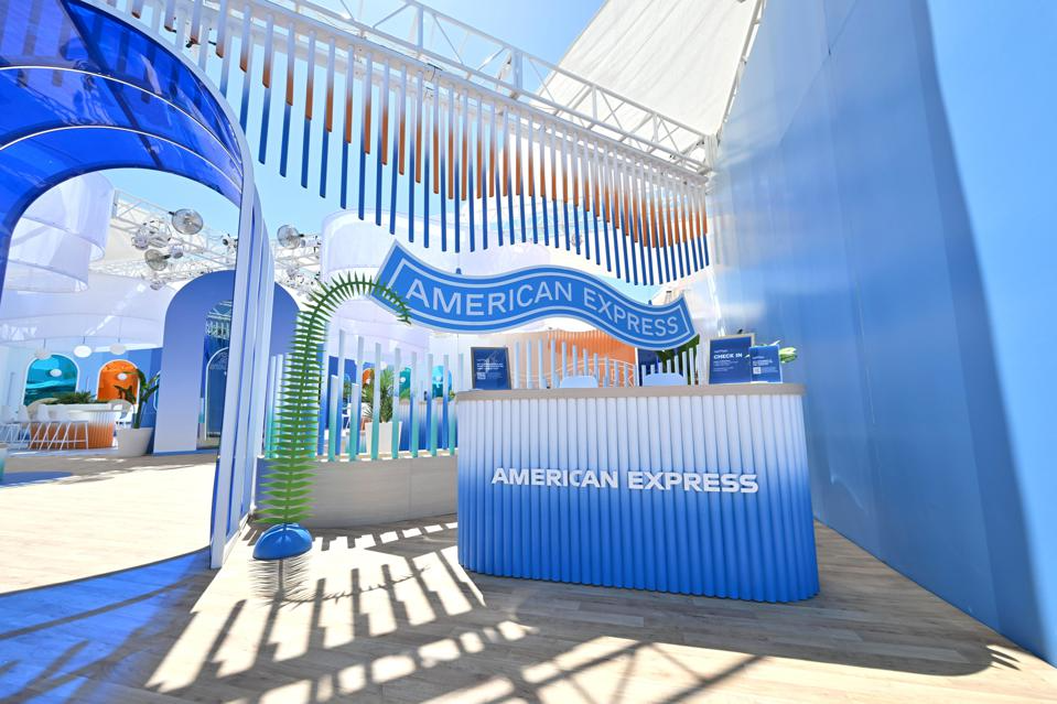 American Express branded booth with a blue and white color scheme, featuring a sign with the American Express logo and a check-in station.