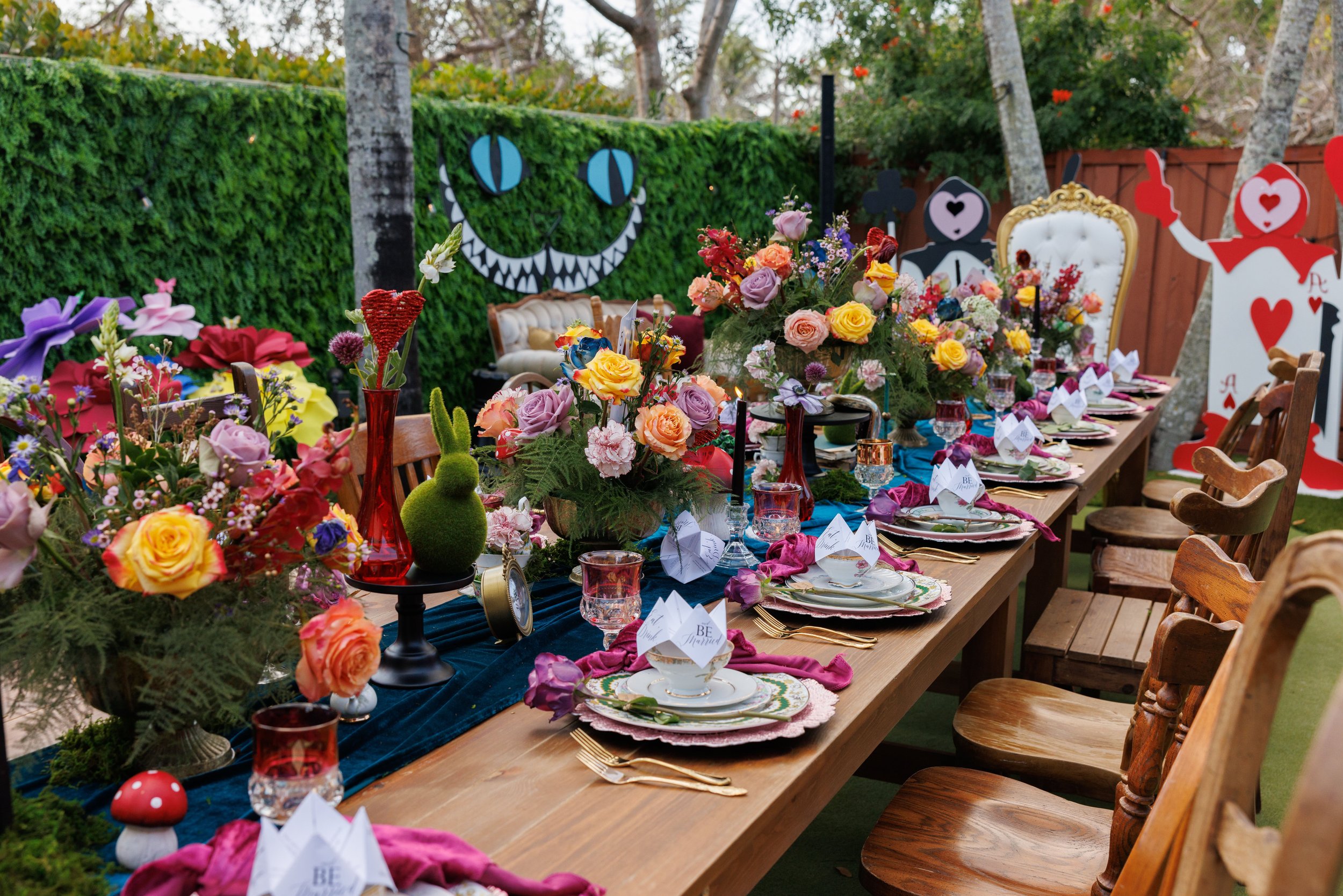 A decorated outdoor table for celebration with colorful flowers, themed decor, and place settings, set among trees and greenery.