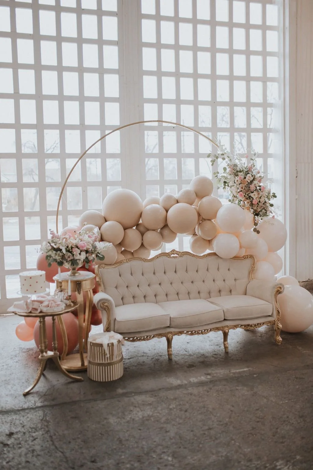 A vintage white tufted sofa with gold trim, decorated with a balloon arch and floral arrangements for a celebration or event.