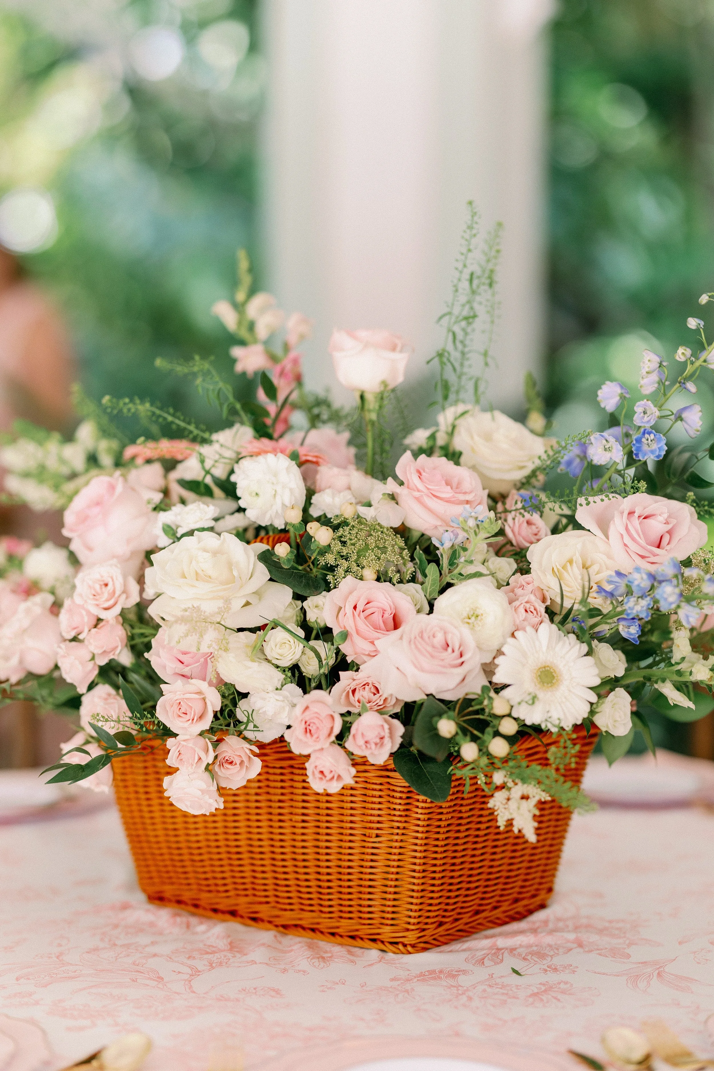 A basket filled with a variety of pink, white, and purple flowers on a pink tablecloth.