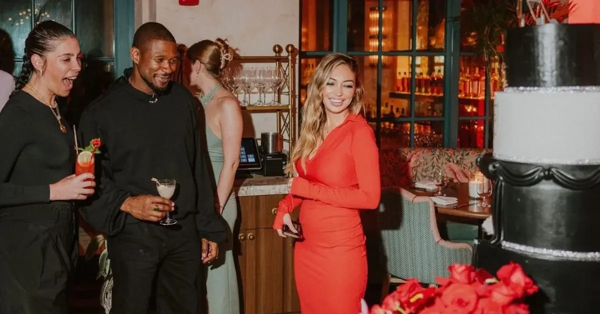 Group of people celebrating at a social event, with a woman in a red dress smiling near a large cake and party decorations.