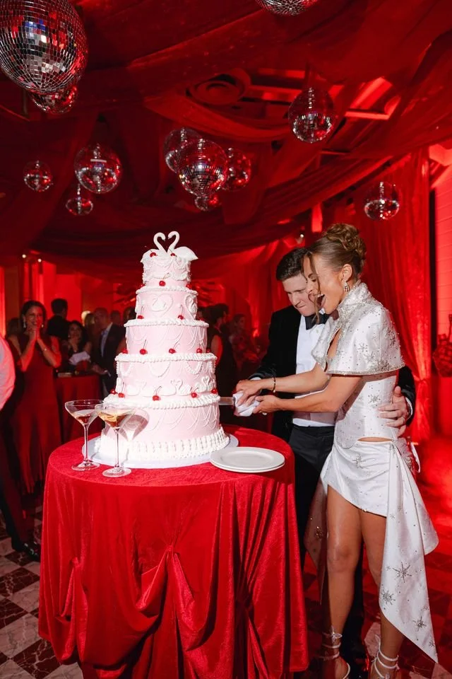 A bride and groom cutting a wedding cake at their celebration, surrounded by guests and festive decorations.