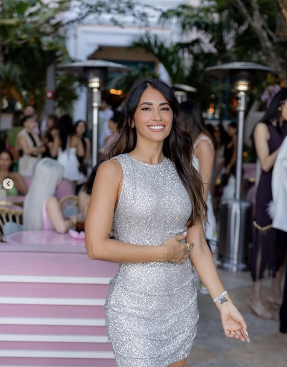 A woman in a sparkling silver dress smiling at an outdoor gathering or event.