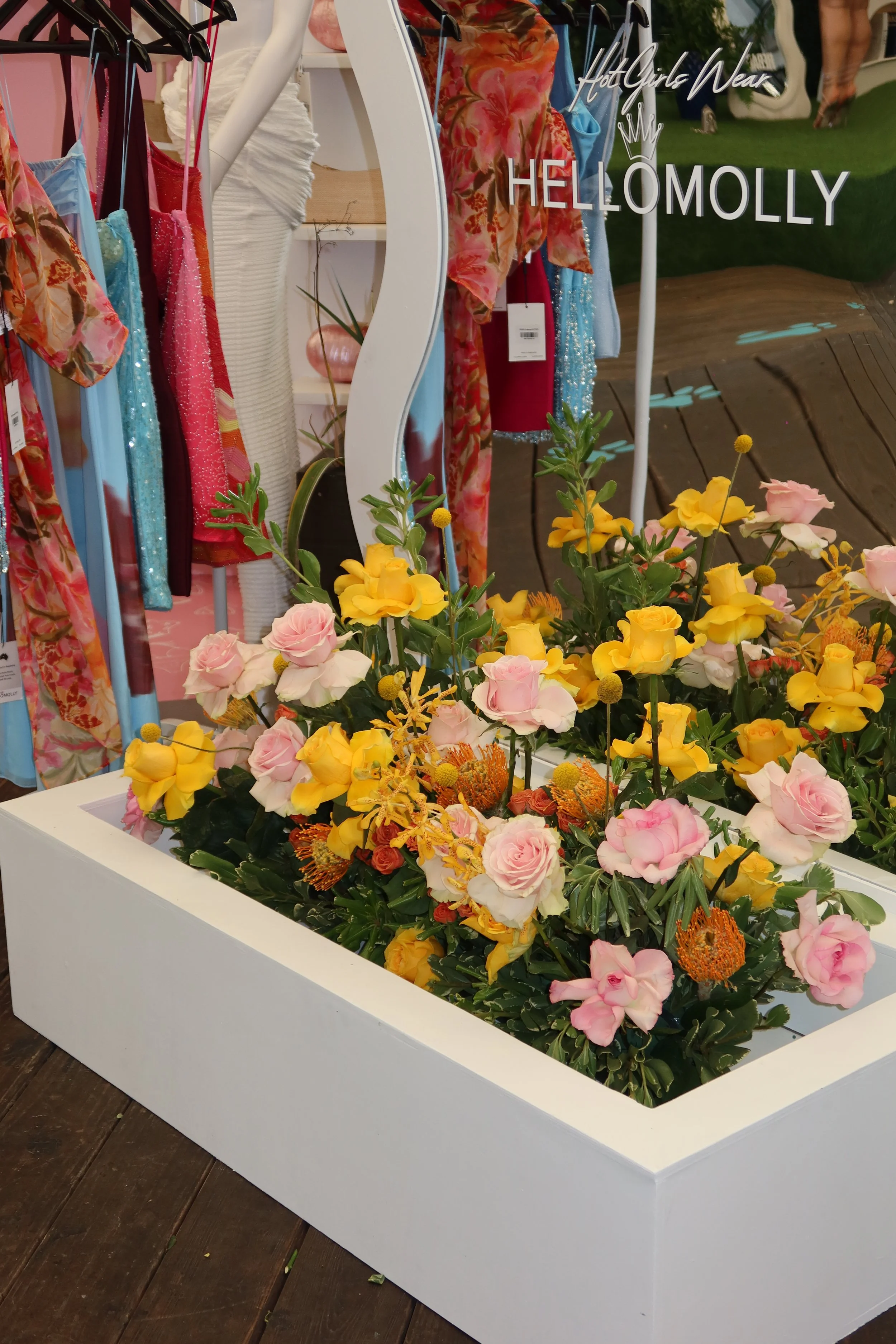 Display of colorful clothing, hats, and flowers in a boutique with a sign reading 'Hot Girls Wear HELLO MOLLY'.