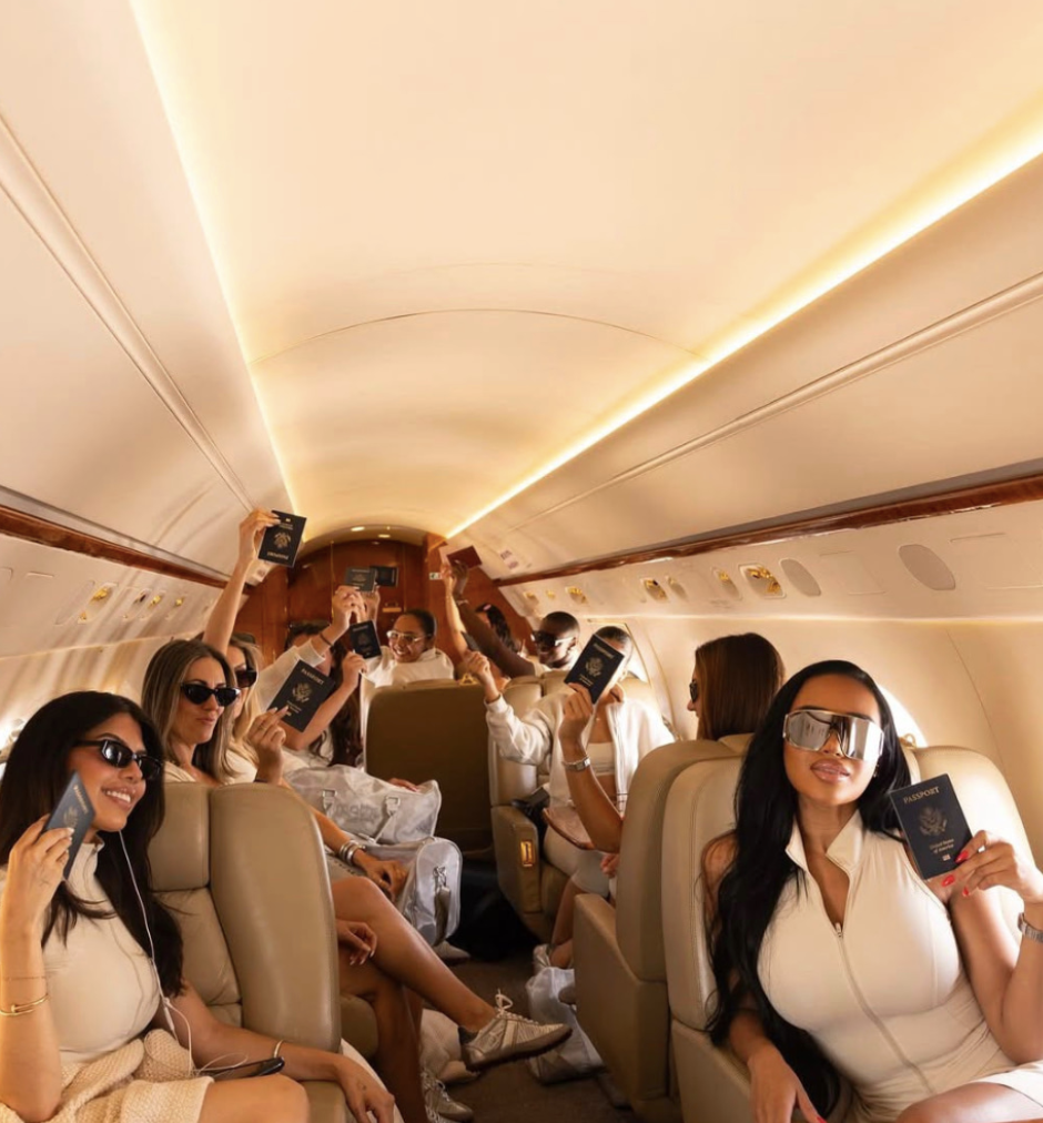 Group of women and men sitting inside an airplane cabin, holding passports, some wearing sunglasses, celebrating and smiling.