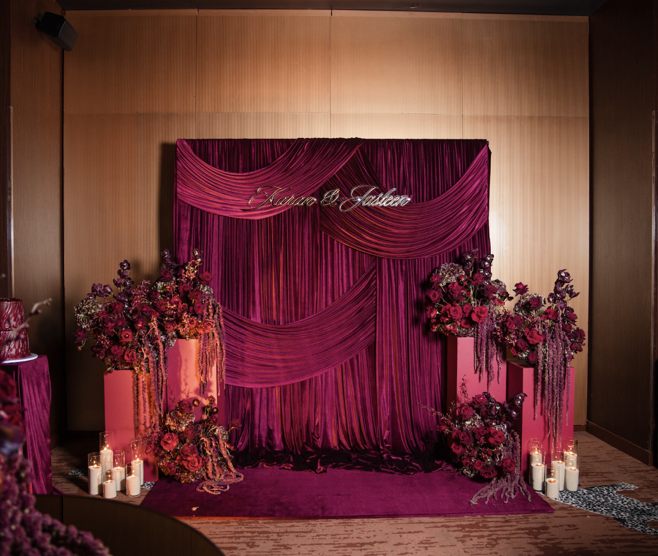 Wedding backdrop with pink drapes and floral arrangements, candles, and the names Karann and Jashlen displayed