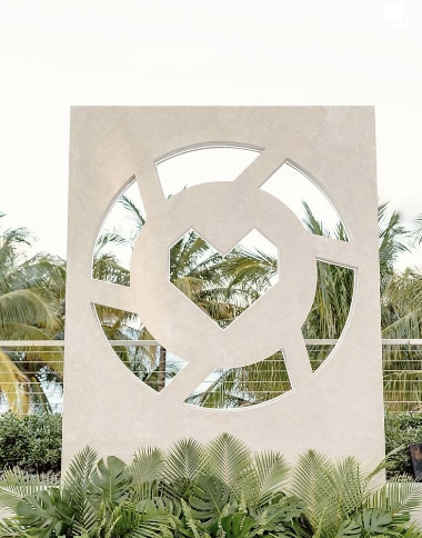 Concrete decorative wall with circular cutouts, overlooking palm trees and lush plants.