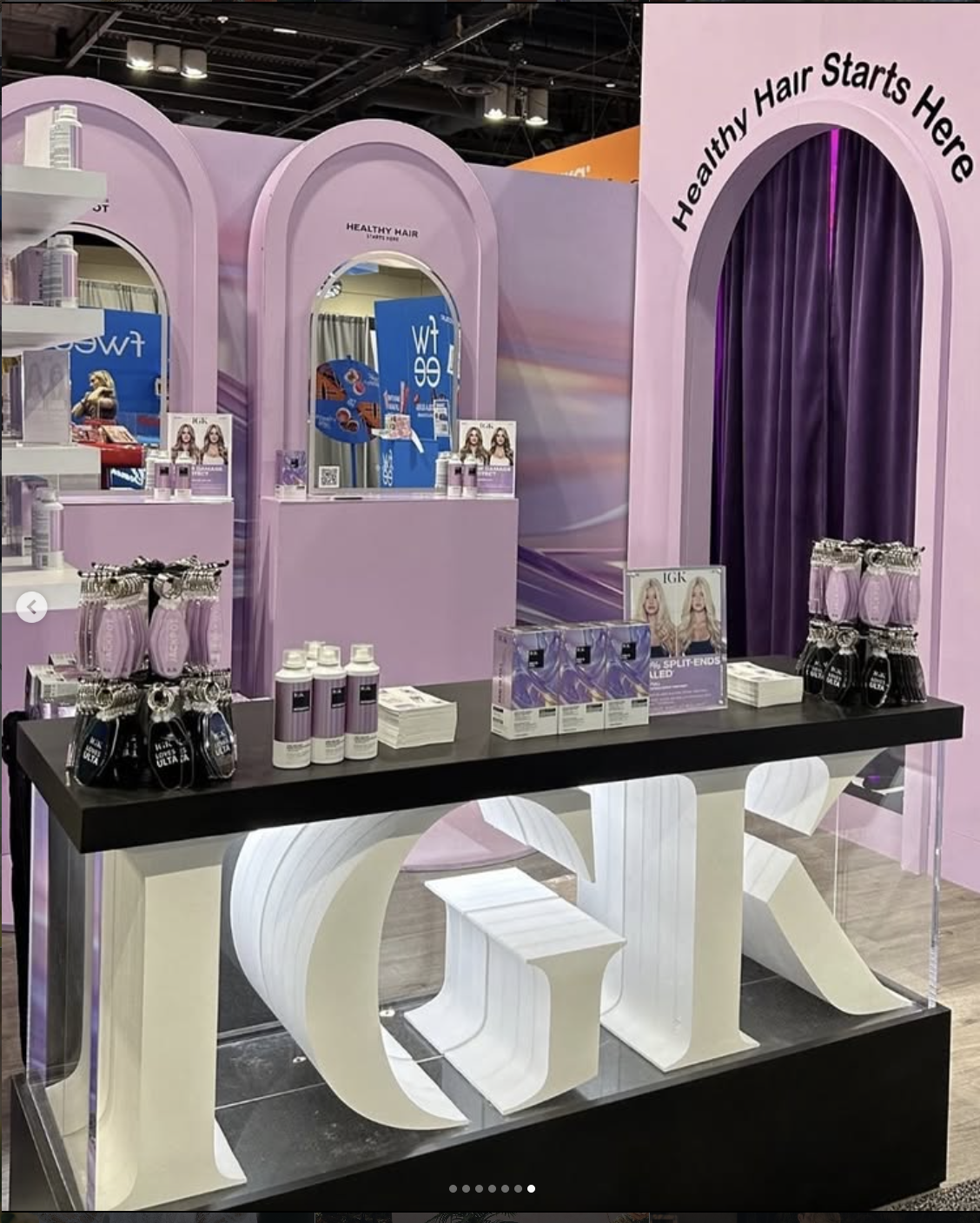 Beauty product display booth with pink and purple decor, featuring shampoos and hair care products, and a large illuminated sign spelling out 'LOVE' in white letters.