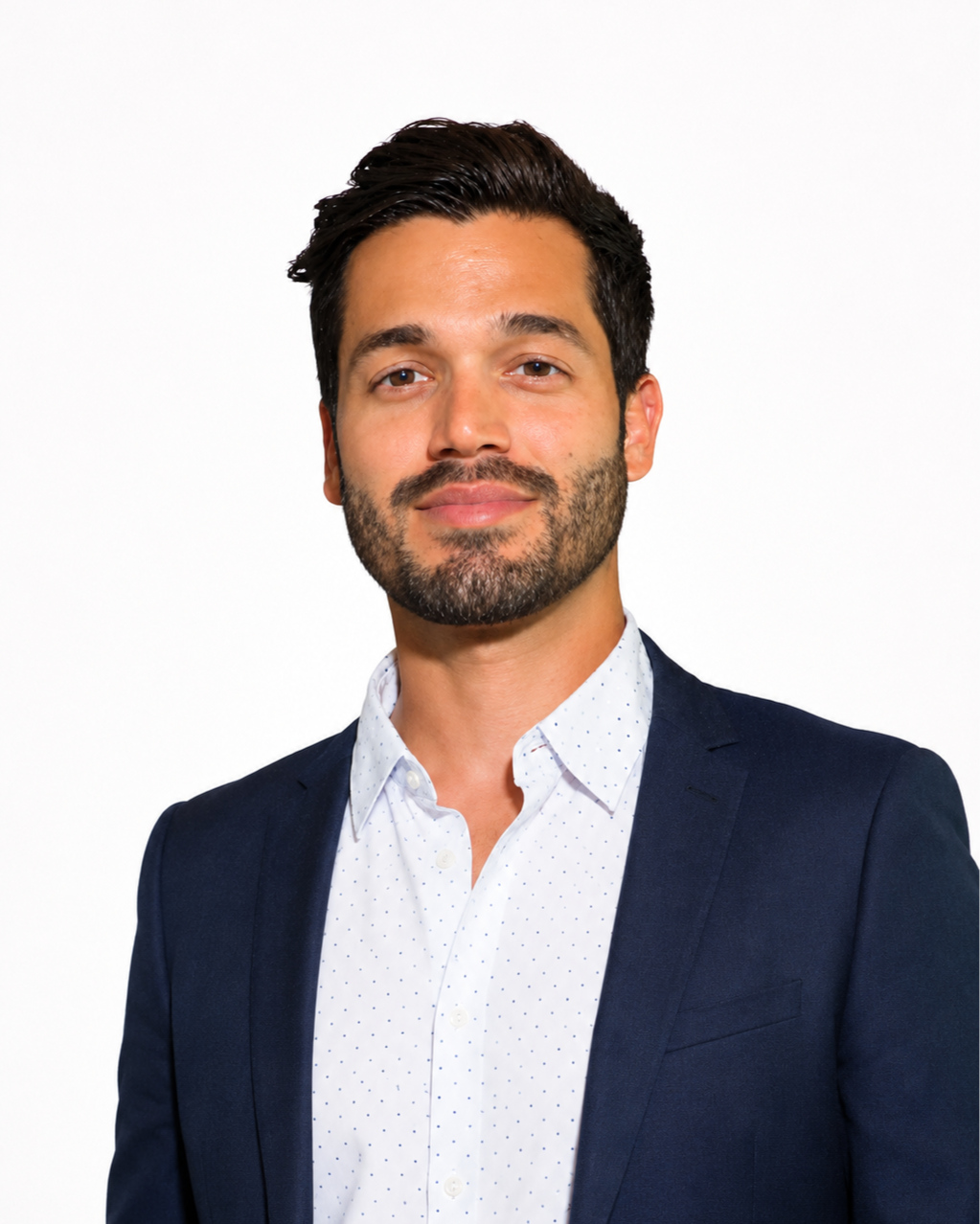 Headshot of a man with dark hair and a beard, wearing a navy blazer and a white shirt with small blue dots, smiling slightly against a plain white background.