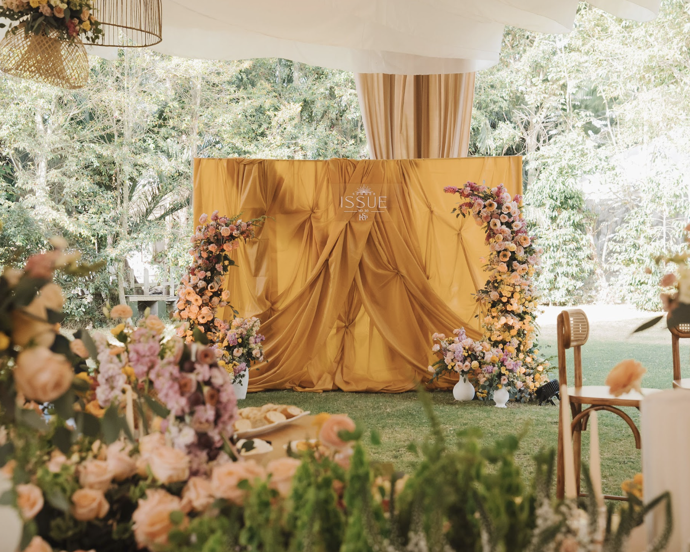 A decorated outdoor event space with a yellow backdrop and floral arrangements, set up for a celebration or wedding.