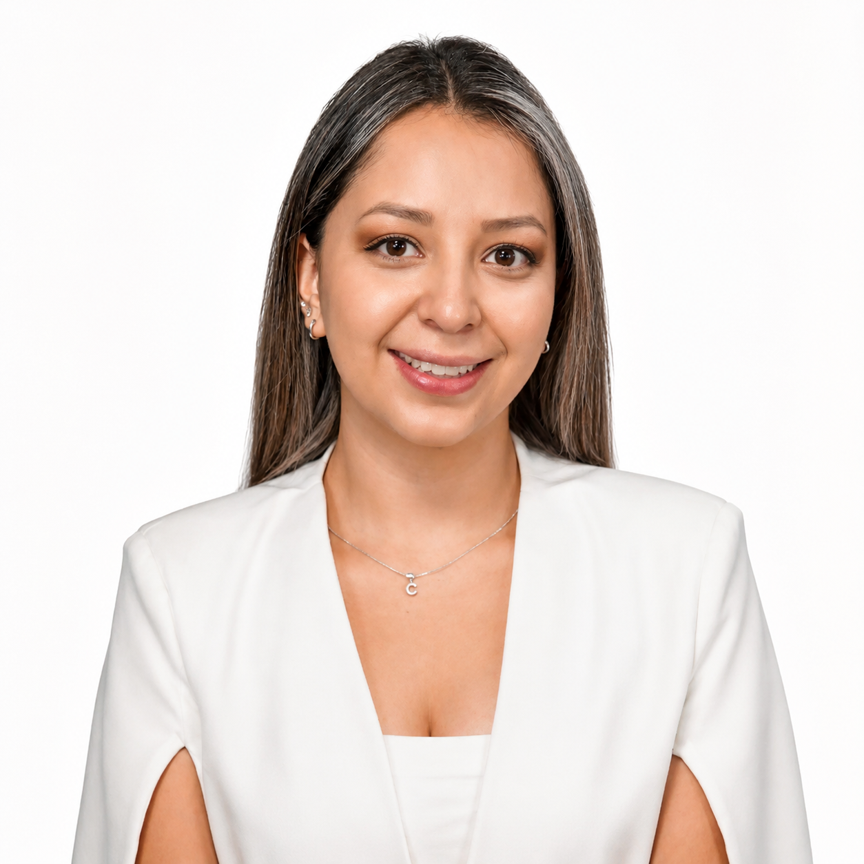 A woman with long brown hair and a friendly smile, wearing a white blazer and silver jewelry, standing against a plain white background.