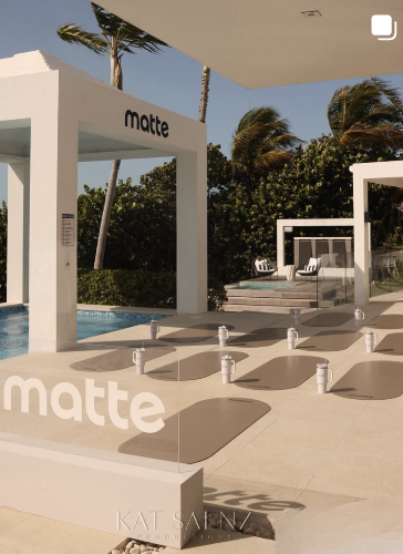 Outdoor pool area with lounge chairs, shaded structures, and palm trees, featuring a display with the word 'matte'.