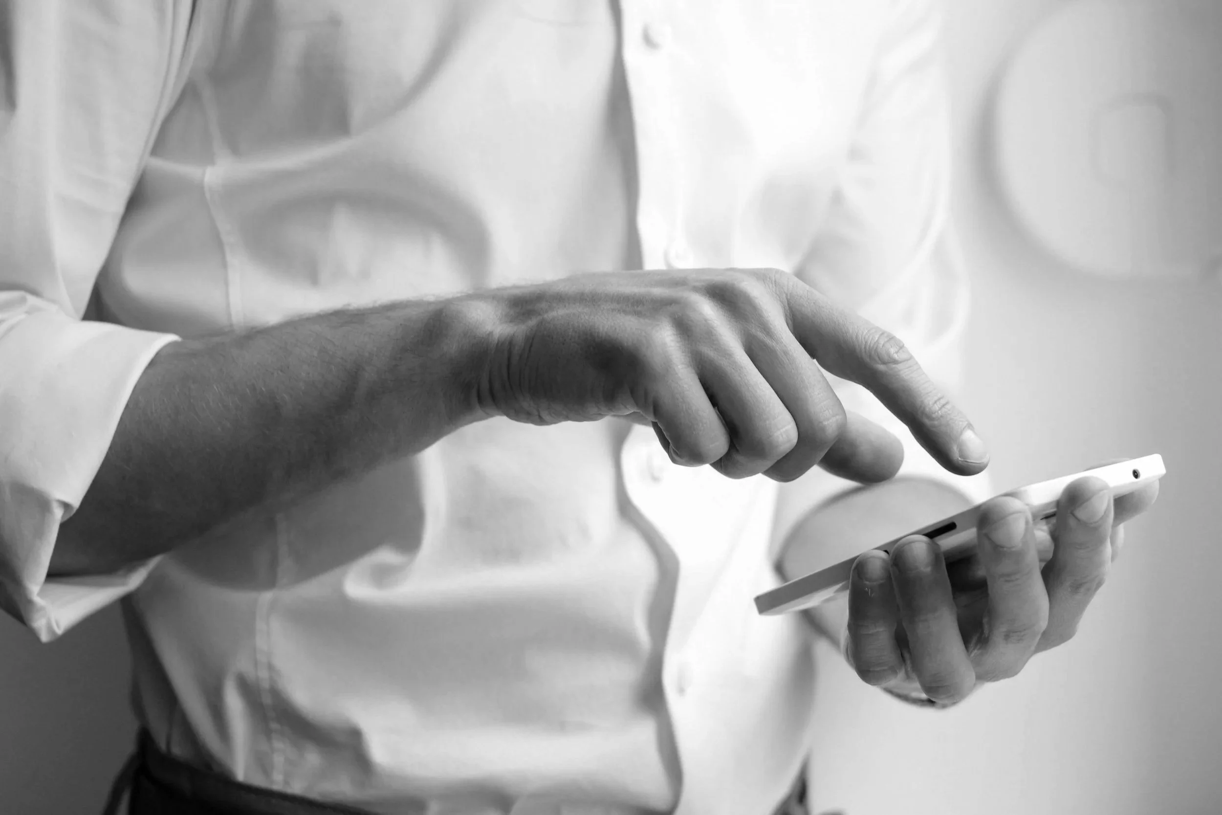Une personne portant une chemise blanche utilise un smartphone, prise en gros plan en noir et blanc.