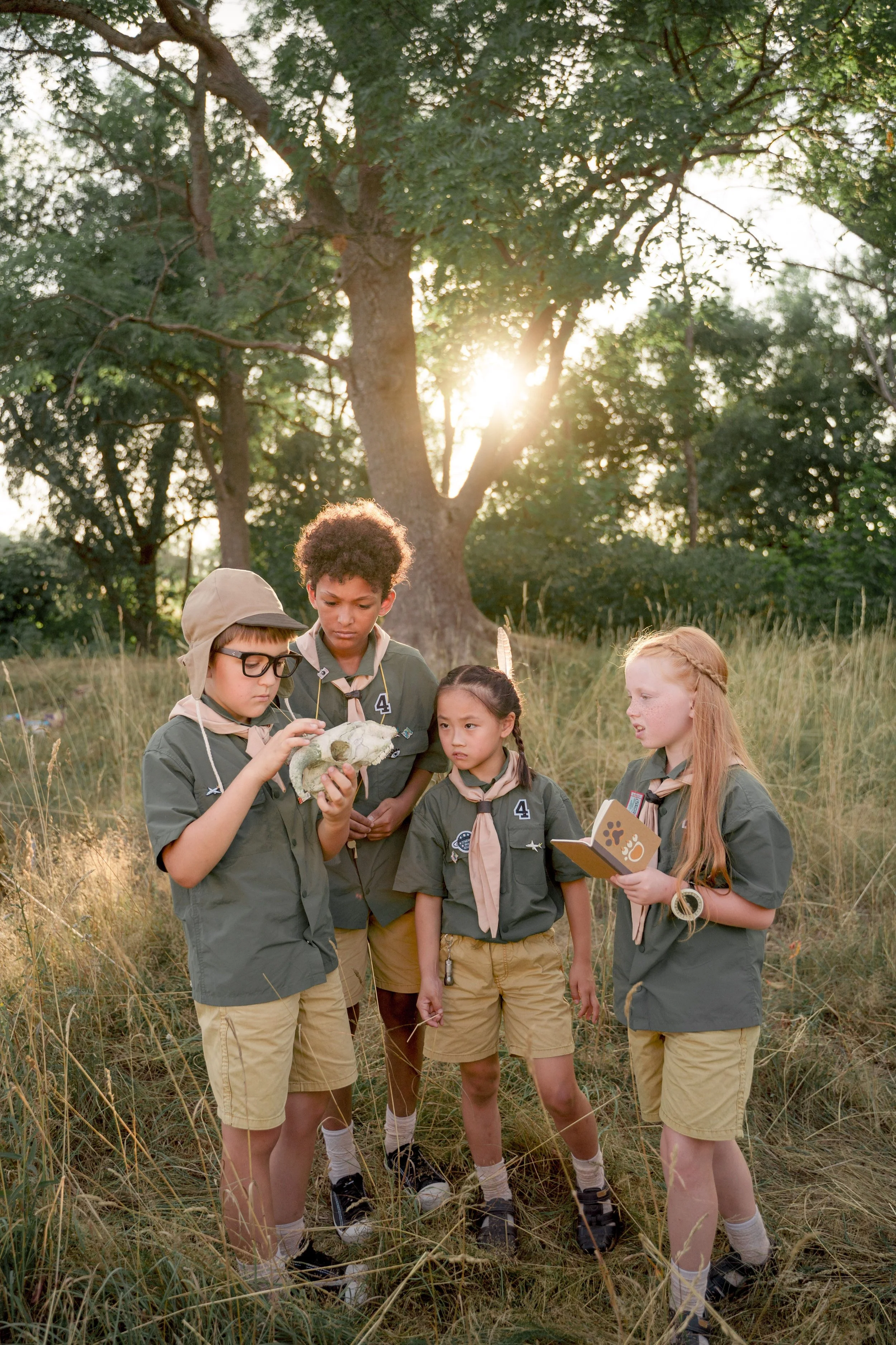 A group of children in scout-style uniforms carefully examine a nature specimen during an outdoor learning activity, highlighting summer camp opportunities and youth development programs that encourage hands-on exploration.