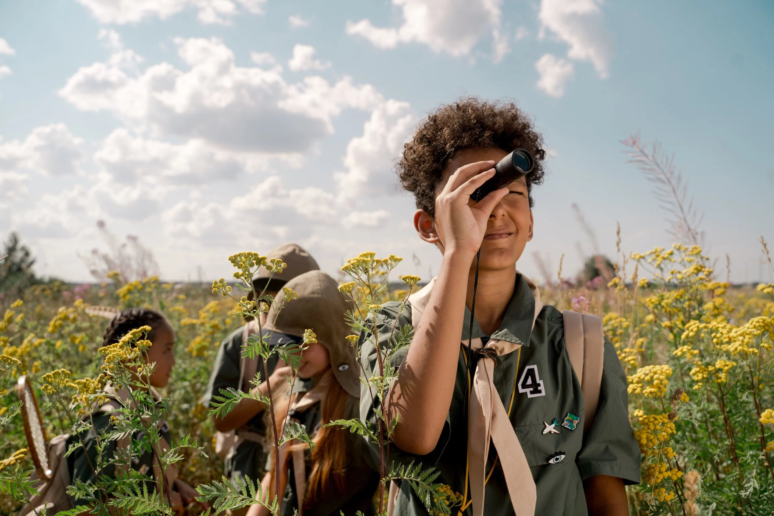 A young camper looks through binoculars during an outdoor adventure, showing the impact of sponsor a child for summer camp and donate for kids initiatives that expand access to camp.