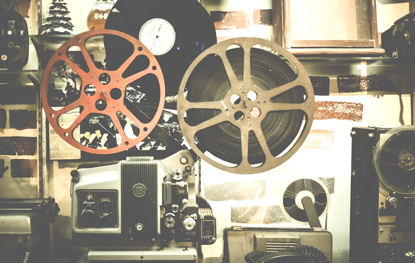 A collection of vintage film projectors and reels on a wall shelf in a workshop or storage room.