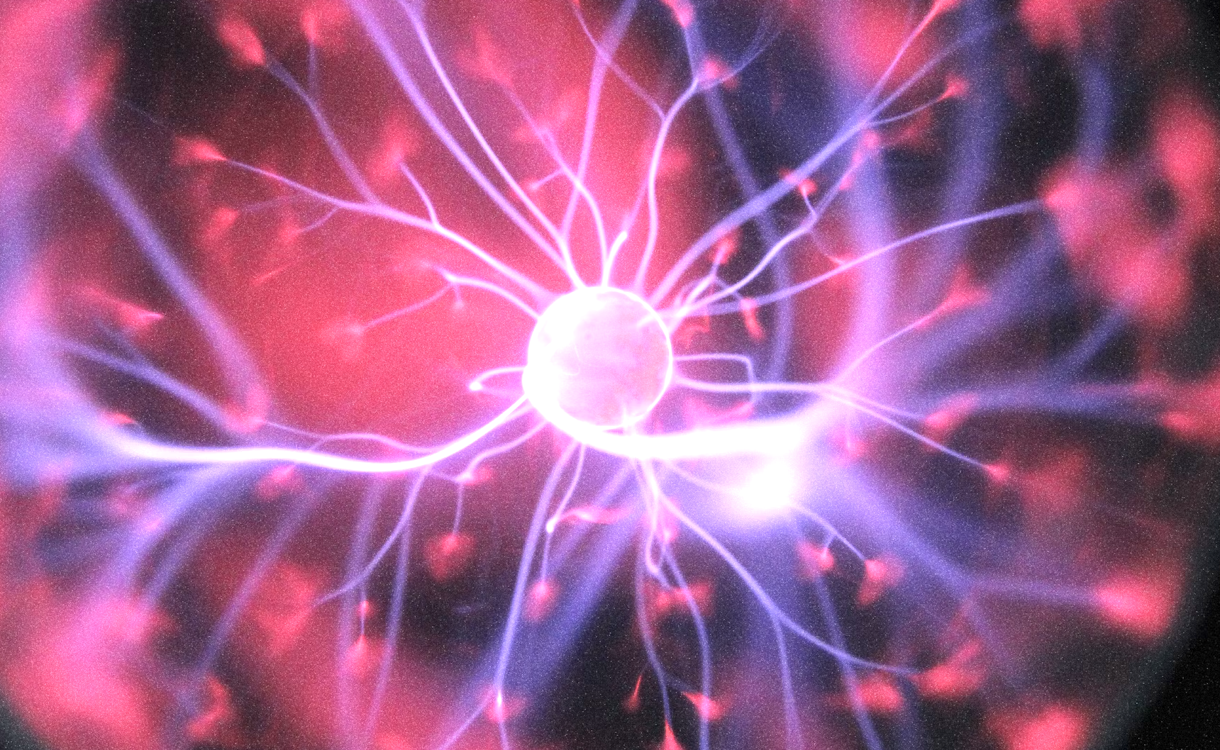 A close-up of a plasma ball with colorful electrical discharges radiating from the center in purple, pink, and blue hues.