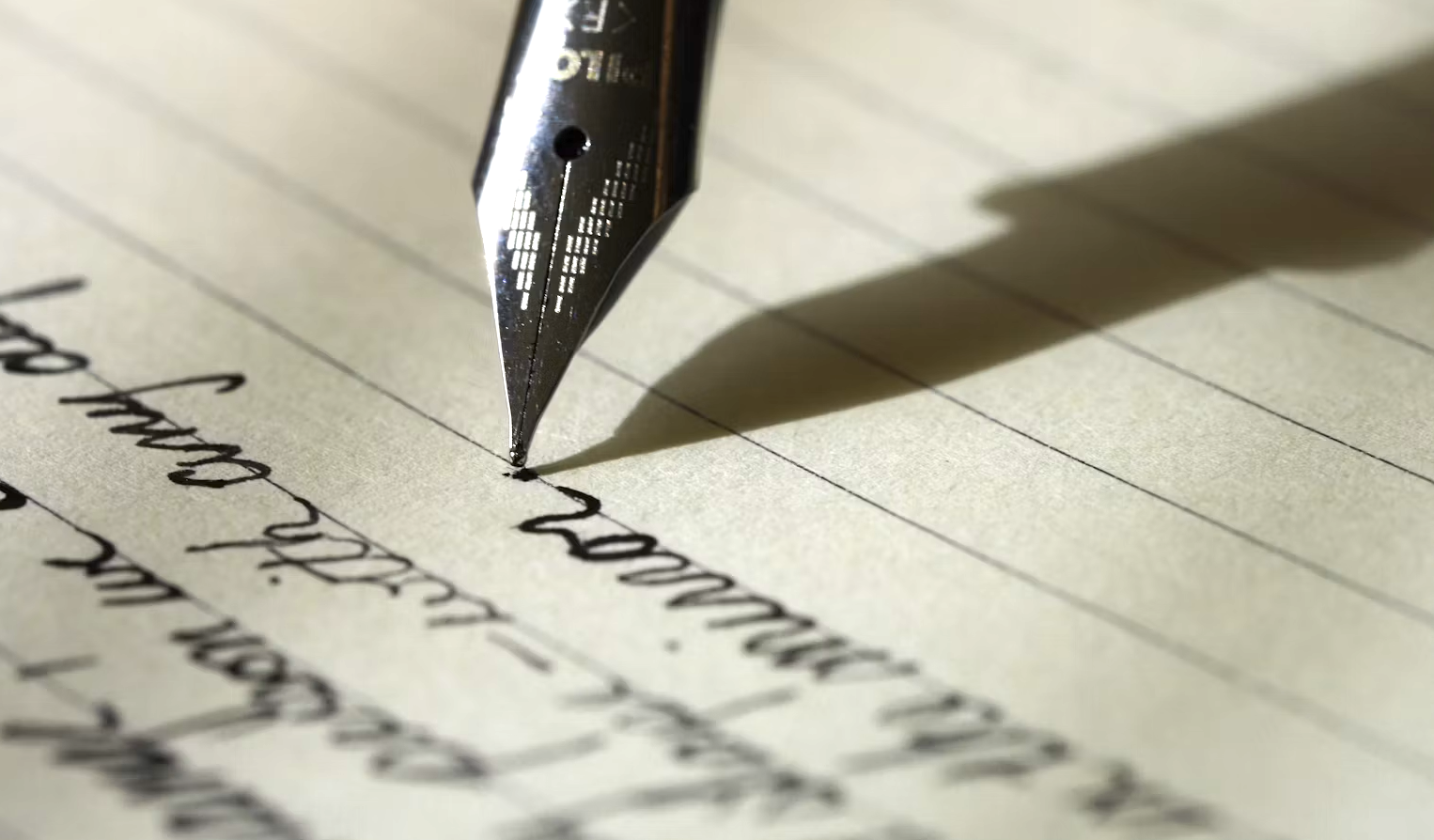 Close-up of a fountain pen writing on a lined sheet of paper with black ink.
