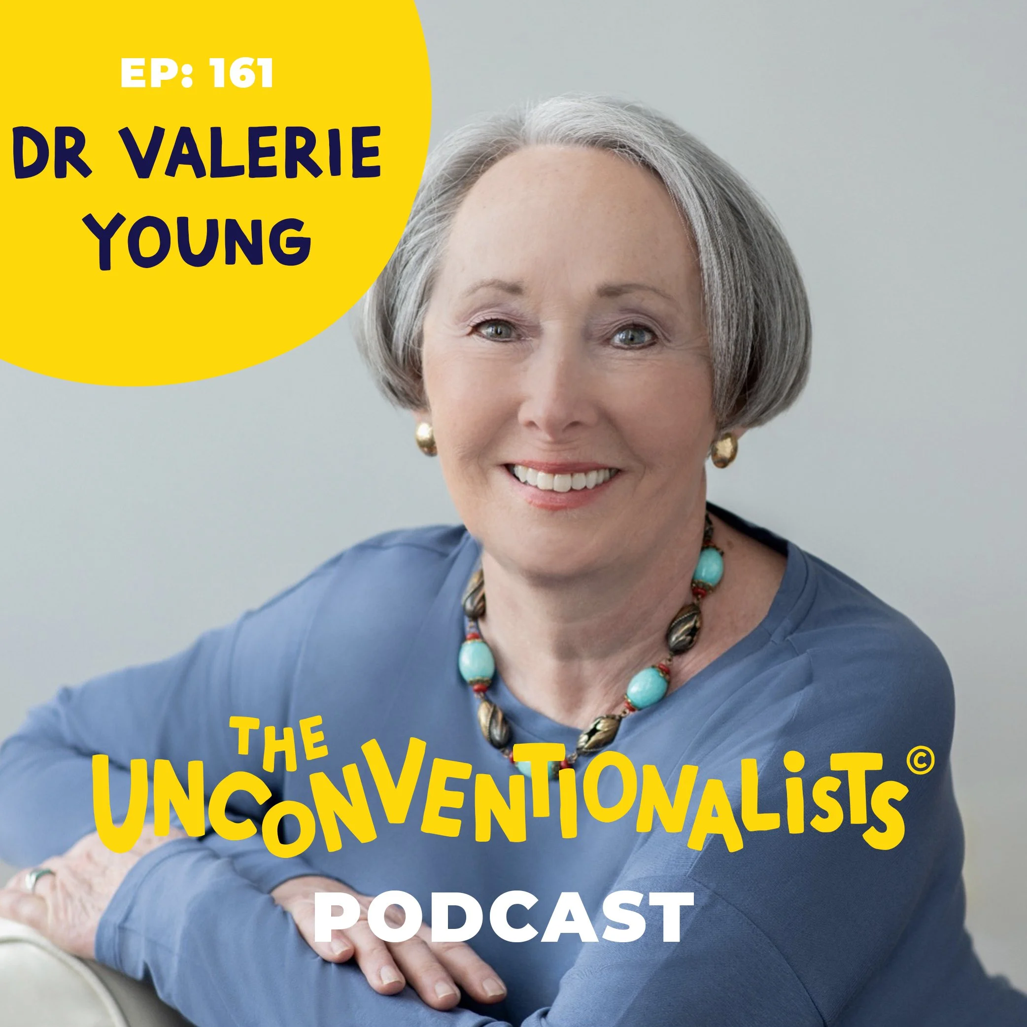 Close-up of a woman with gray hair smiling, wearing earrings and a turquoise necklace, holding a sign that reads 'The Unconventionalist Podcast' with yellow text on a dark background.