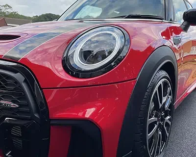 Close-up of the front side of a red Mini Cooper car, showing the headlight, wheel, and part of the hood.