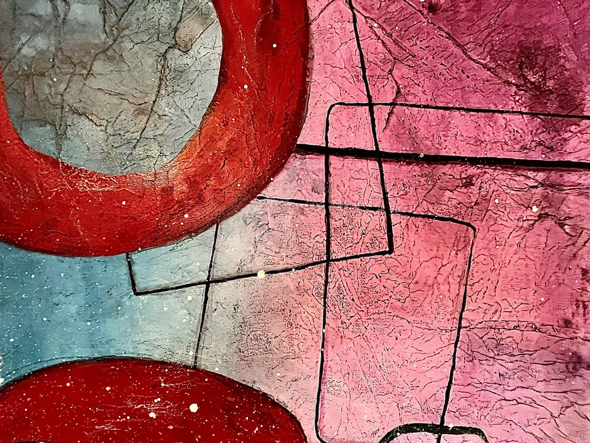 Close-up of colorful abstract graffiti art on a textured wall, featuring pink, gray, and red sections with black lines and crack patterns.