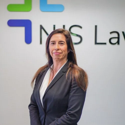 A woman in a dark suit standing in front of a wall with the NIS Law logo.