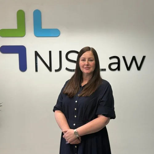 Woman in a dark dress standing in front of a wall with the NJS Law logo.