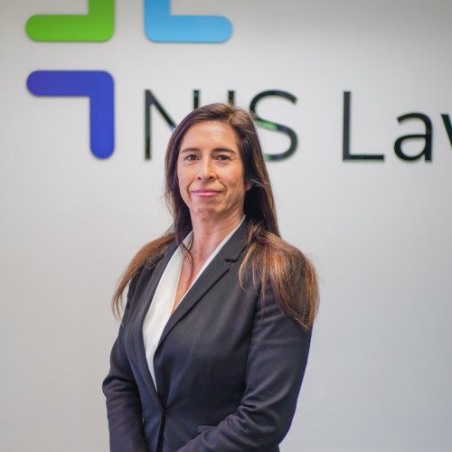 A woman in professional attire standing in front of a wall with a logo and text that reads 'NHS Law'.