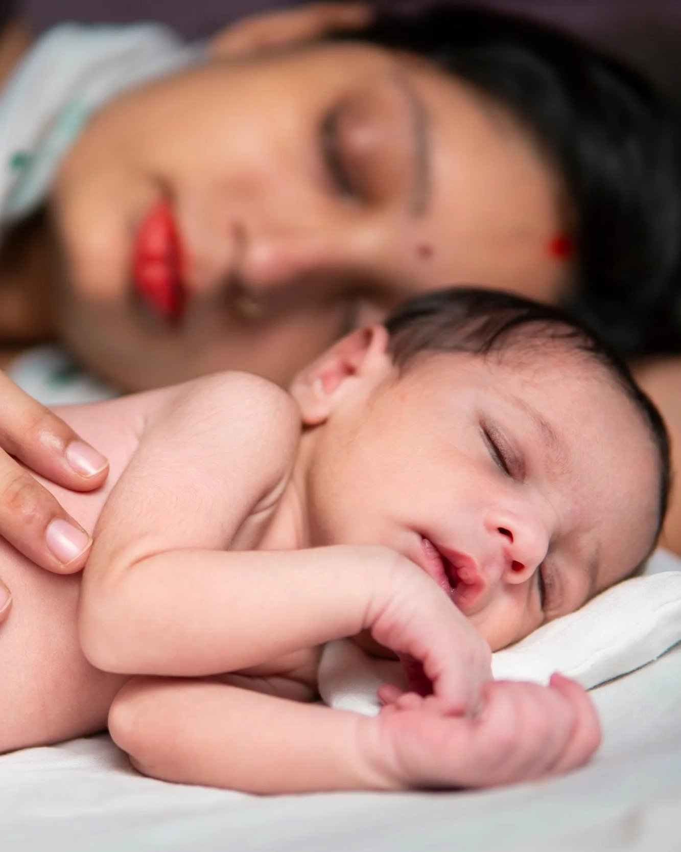 A mother and her young child, both with eyes closed, resting peacefully as they cuddle together on a soft surface.