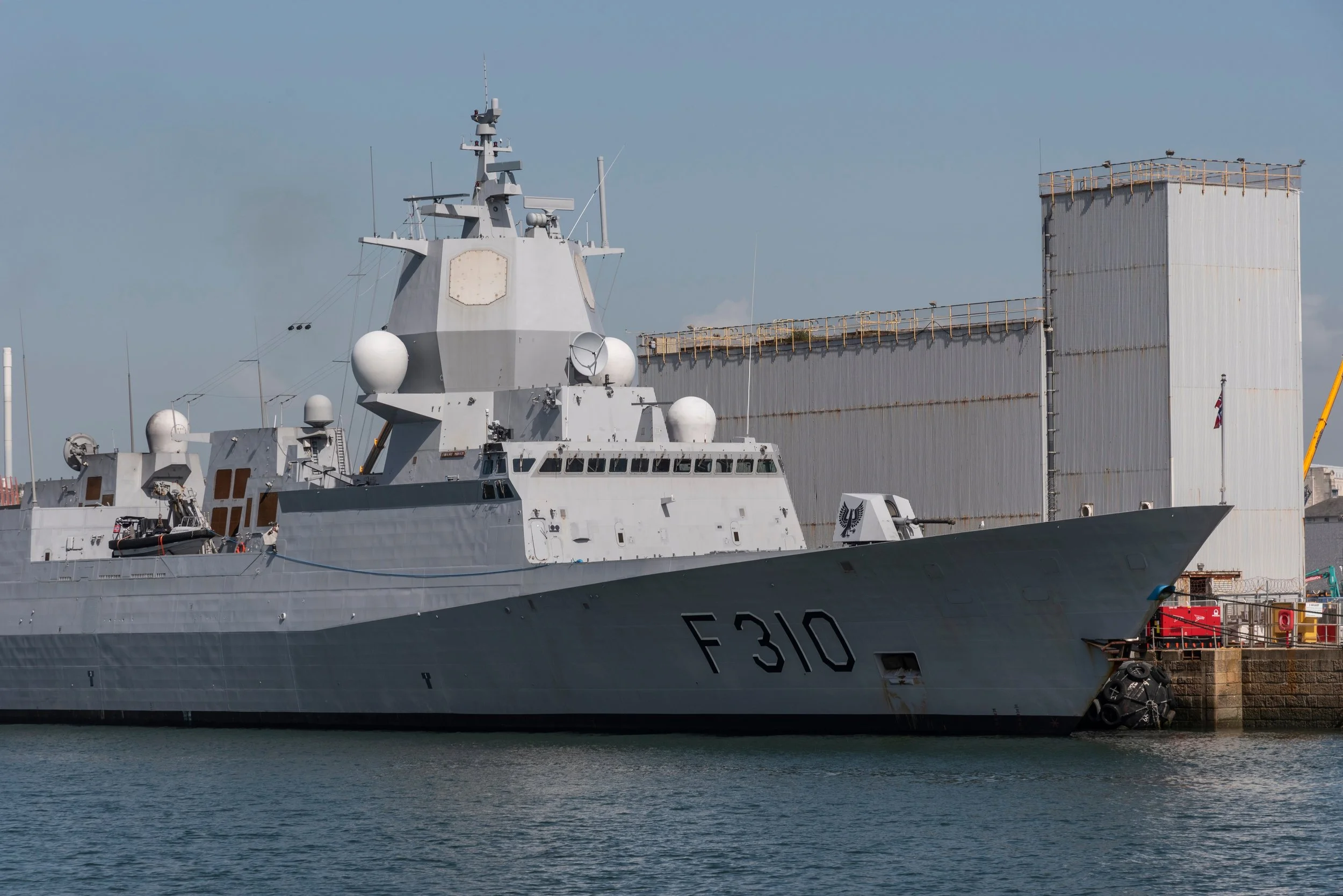 A large grey military ship docked in a harbor with a building in the background.
